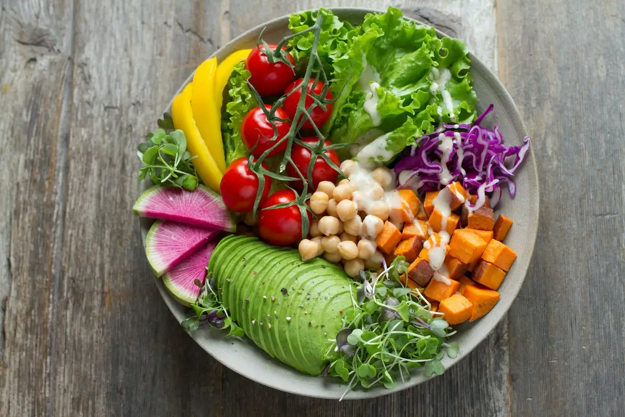 A bowl of mixed vegetables, chickpeas, avocado and leafy greens arranged on a wooden table